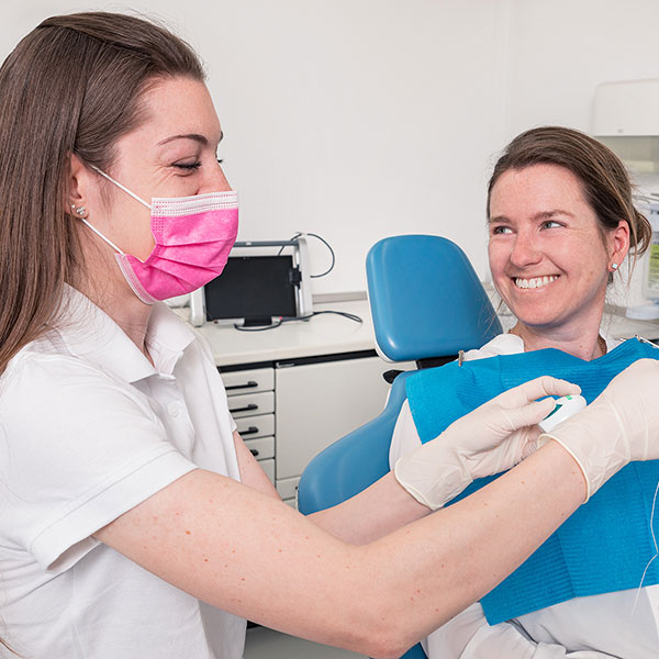 Zahnarzt-Dachau---Zahnarztpraxis-Dr.-Gitt-bei-der-Prophylaxe-1 Zahnarzt Dachau - Eine freundlich lächelnde Prophylaxeassistentin in weißer Kleidung führt Prophylaxe bei Patientin im blauen Zahnarztstuhl durch