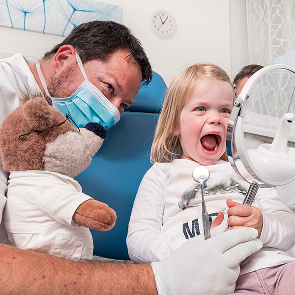 Familienzahnarzt-Dr.Gitt-quad Familienzahnarzt Dr. Gitt in Dachau erklärt einer kleinen Patientin mit Hilfe eines Spiegels und des Stoffbärs Dr. Bär.
