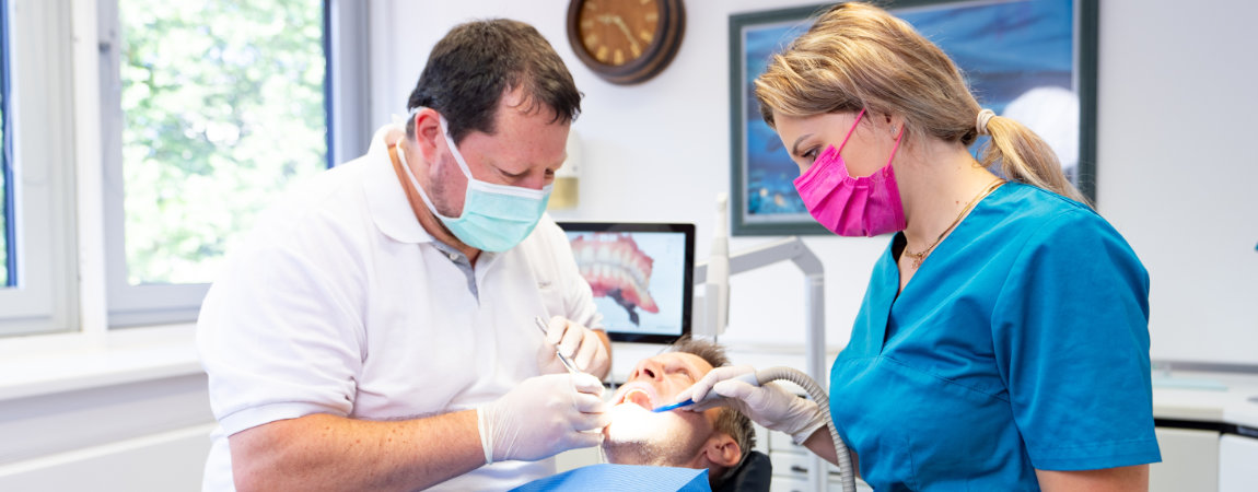 Leistungen-Zahnarzt-Dr.-Gitt 5 Der Dachauer Zahnarzt Dr. Gitt und Assistentin behandeln einen Patienten auf dem blauen Behandlungsstuhl.