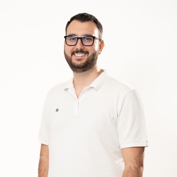 Neuer Zahnarzt 3 Dr. Vasileiadis--Zahnarzt in Dachau, lächelnd, mit Bart und Brille, in weißem Kittel.