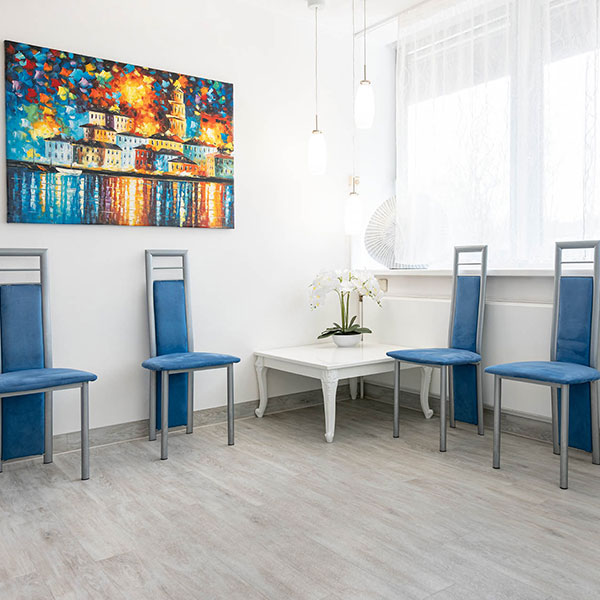 Zahnarzt-Dachau---Wartezimmer Zahnarzt Dachau - Das Wartezimmer für die Patienten mit blauen Stühlen, weißem Tisch und Orchidee, modernes Gemälde an der Wand.